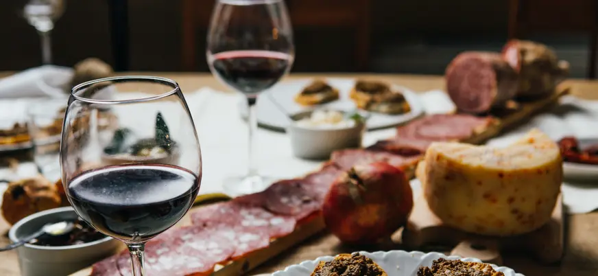 Mesa con una variedad de embutidos, quesos y copas de vino tinto de Chianti