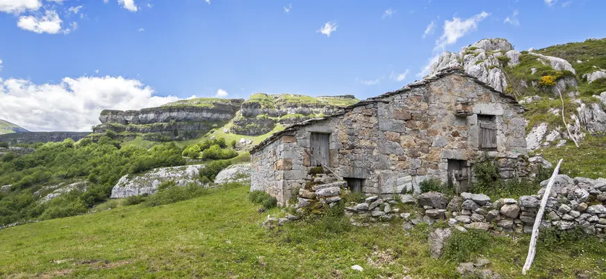 Cabaña de piedra tradicional en un valle verde, rodeada de montañas y naturaleza en Cantabria.