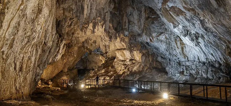 Interior de la cueva Cullalvera iluminado, con estalactitas y pasarela para visitantes en un amplio espacio