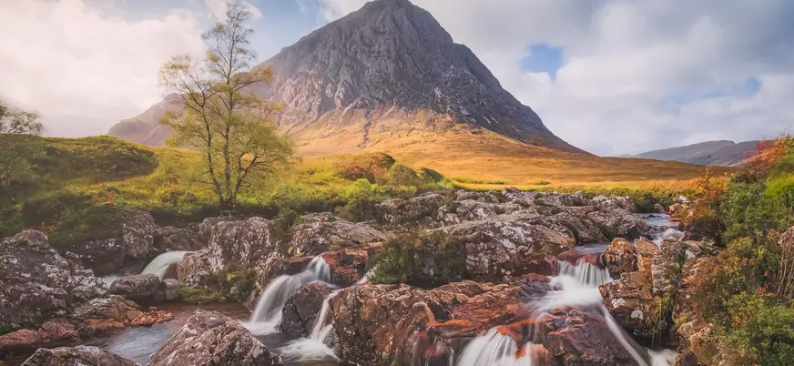 Paisaje de las tierras altas, con pequeños saltos de agua de un arroyo, campos dorados y montañas