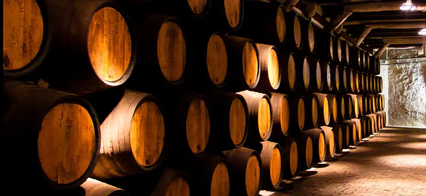 Sala de barricas de vino apiladas en una bodega iluminada cálidamente.