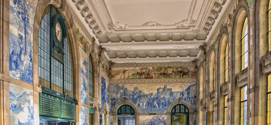 Interior de São Bento con murales de azulejos azules y gran reloj.
