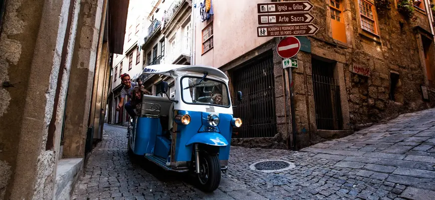Tuk tuk azul recorriendo una calle estrecha empedrada en el casco histórico de Oporto.