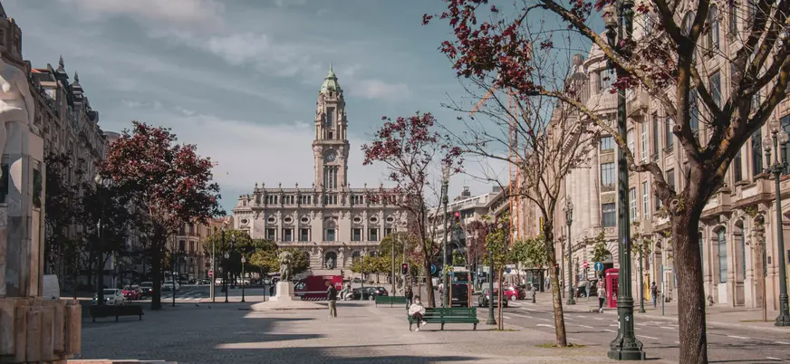 Plaza en Oporto con árboles y el edificio del ayuntamiento al fondo en un día despejado.