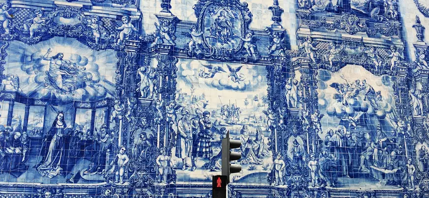 Mural de azulejos azules en Oporto con escenas religiosas y un semáforo en primer plano.