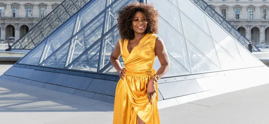 Persona con vestido largo amarillo posando frente a la Pirámide del Louvre en París.