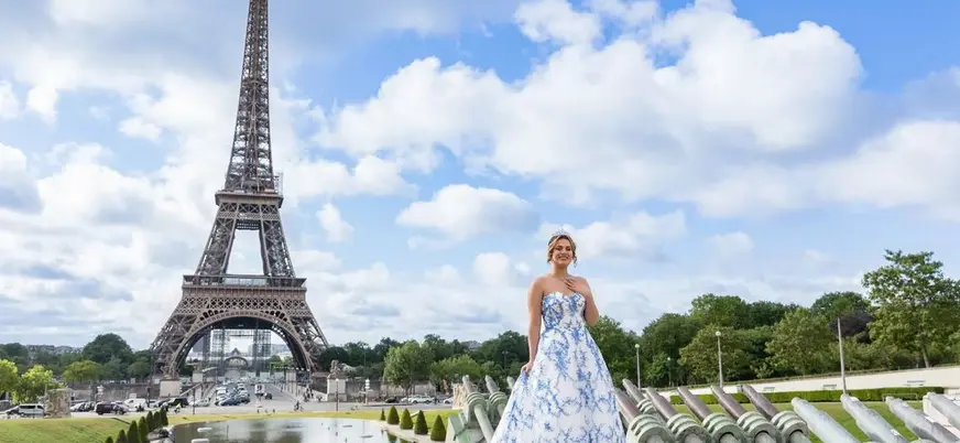 Persona con vestido largo azul y blanco posando frente a la Torre Eiffel en París.