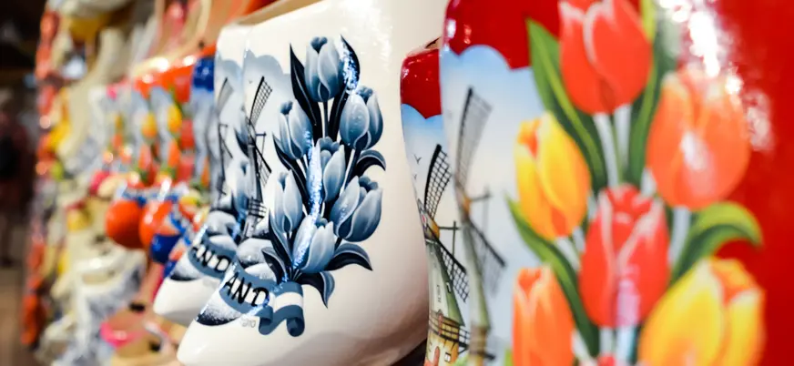 Zuecos de madera pintados a mano con diseños de tulipanes y molinos de viento, típicos de la artesanía holandesa, expuestos en una tienda.