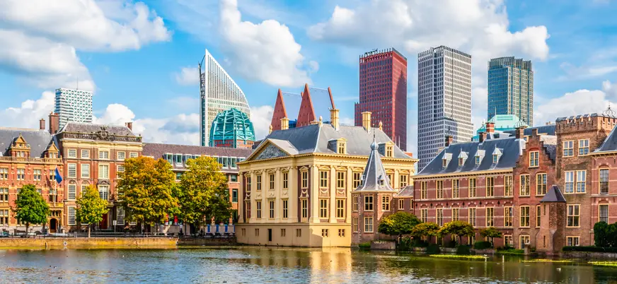 Vista panorámica del Hofvijver en La Haya, Países Bajos, con edificios históricos rodeando el estanque en primer plano y modernos rascacielos de cristal y metal al fondo