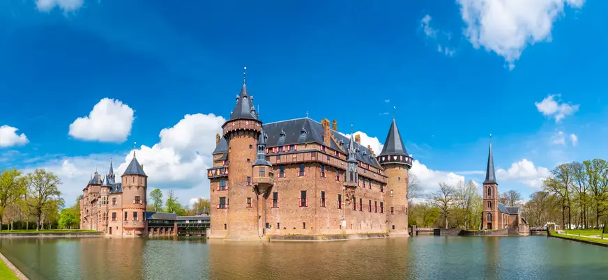 Vista panorámica del Castillo de Haar en los Países Bajos, rodeado por un foso de agua, con torres y muros de ladrillo rojo. 