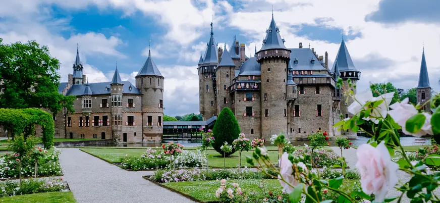 Jardines floridos con rosas frente al Castillo de Haar en los Países Bajos, con el majestuoso edificio medieval de torres y muros de ladrillo en el fondo. y un cielo parcialmente nublado