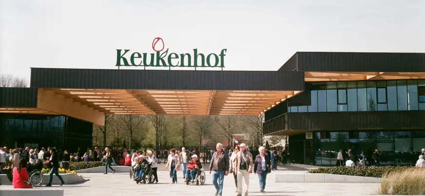 Entrada principal del parque Keukenhof en los Países Bajos, con varias personas caminando y disfrutando del lugar en un día soleado, y el letrero "Keukenhof" visible sobre la entrada.