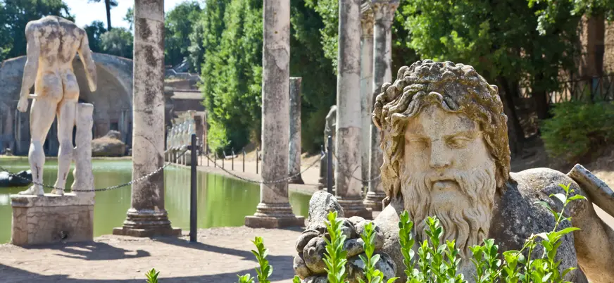 Estatuas y columnas romanas junto a estanque rodeado de vegetación en Villa Adriana, Tívoli.