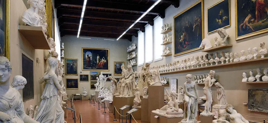 Sala del museo en Florencia con numerosas esculturas clásicas de mármol, bustos alineados en estanterías y grandes pinturas renacentistas colgadas en las paredes.