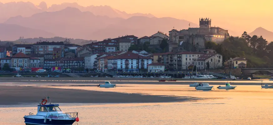 Vista de San Vicente de la Barquera al atardecer, con la iglesia y el castillo sobre el casco histórico junto a la ría.