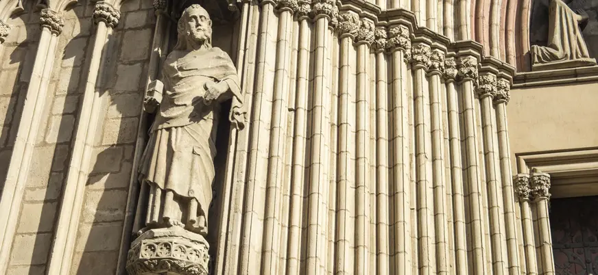 Escultura de figura religiosa en la fachada gótica de la Catedral de Santa María del Mar en Barcelona, con columnas ornamentadas.