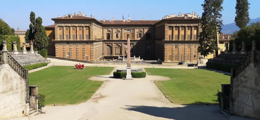 Vista frontal del Palacio Pitti en Florencia, Italia, con su arquitectura renacentista, amplio patio central, jardines simétricos y un obelisco en el centro.