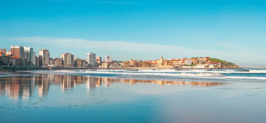 Vista panorámica de la playa de San Lorenzo en Gijón, con el barrio de Cimavilla y la iglesia de San Pedro al fondo