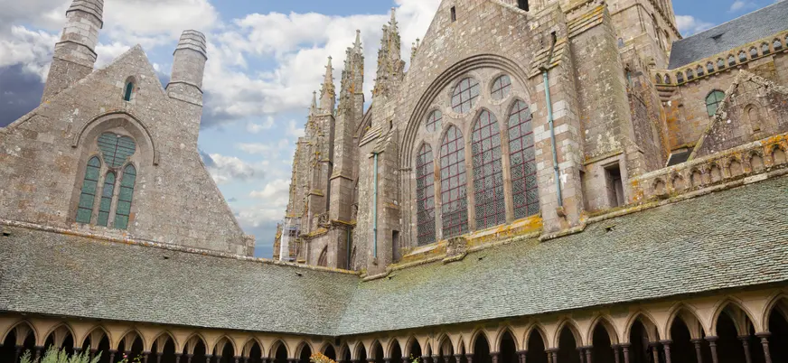 Claustro y fachada gótica de la abadía del Mont Saint-Michel en Normandía, Francia, con arcos y ventanales históricos.