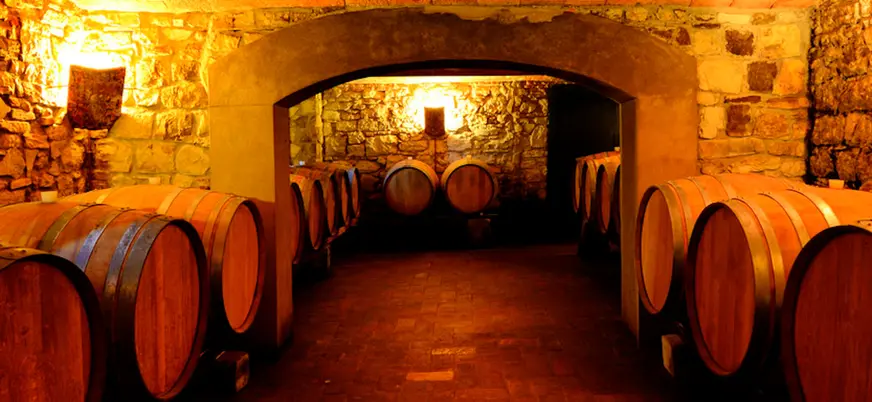 Bodega tradicional en la Toscana, Italia, con barricas de madera alineadas en una sala de piedra iluminada con luz cálida.