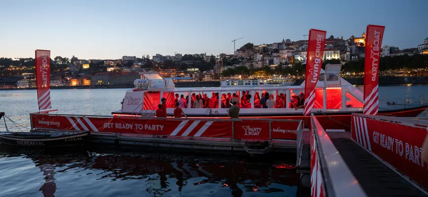 Barco de fiesta iluminado al anochecer frente a la ciudad de Oporto.