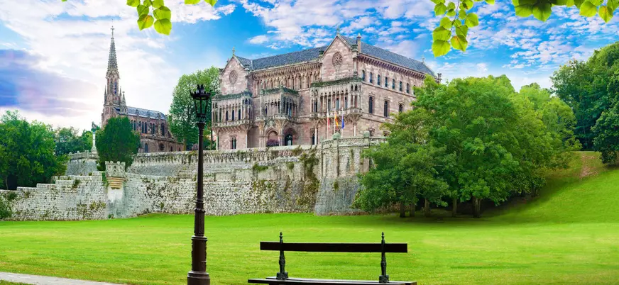 Palacio de Sobrellano y su entorno verde en Comillas, Cantabria, con cielo azul y jardines cuidados.