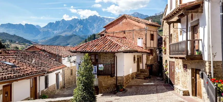 Calles de Potes con casas de piedra y los Picos de Europa al fondo.