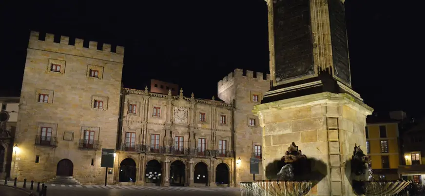 Vista nocturna del Palacio de Revillagigedo y la fuente del monumento a Pelayo iluminados en la plaza principal de Gijón