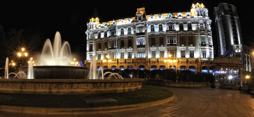 Fuente y edificio histórico de la Plaza de la Escandalera en Oviedo iluminados de noche, uno de los puntos más icónicos de la ciudad.