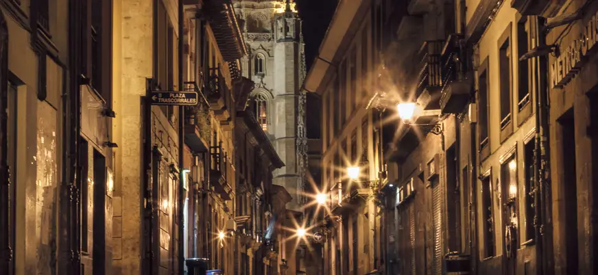Fachada del Ayuntamiento de Oviedo iluminada de noche, con reflejos sobre el suelo mojado en la Plaza de la Constitución.