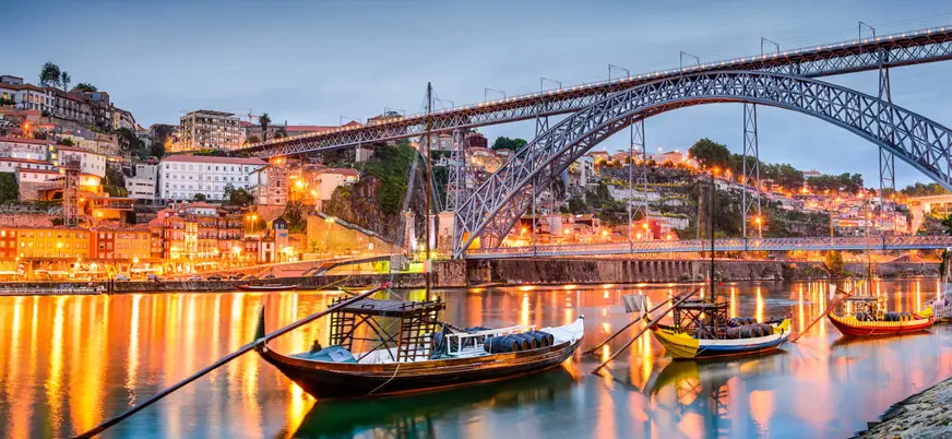 Barcos frente al Puente Luis I iluminado en Oporto