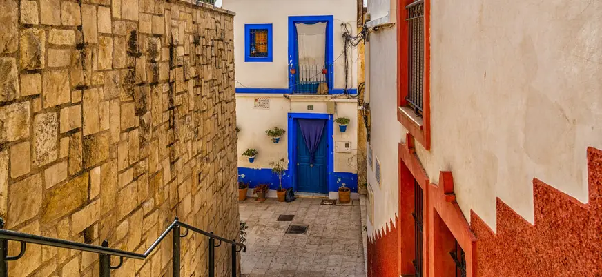 Calle estrecha con fachada blanca y detalles azules en el barrio de Santa Cruz, Alicante