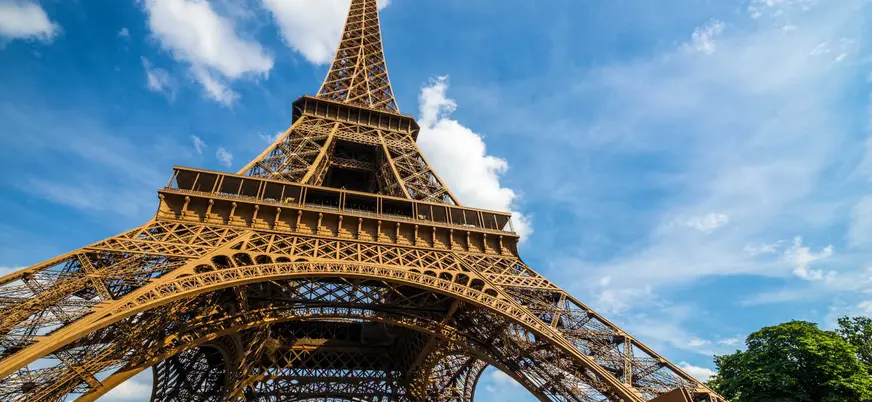 Vista desde abajo de la Torre Eiffel con cielo azul y flores en primer plano.