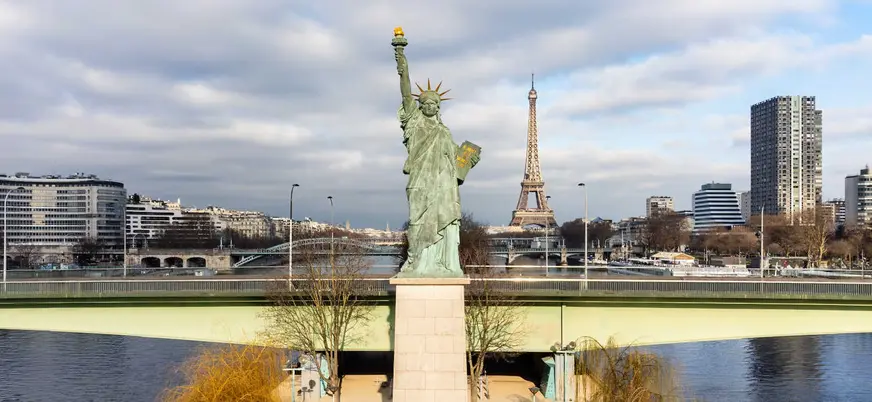 Estatua de la Libertad en París con la Torre Eiffel al fondo junto al río Sena.