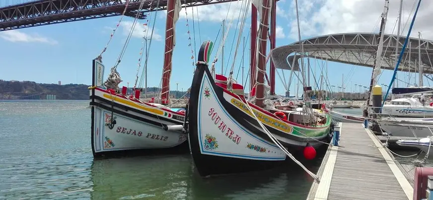 Moliceiros tradicionales junto al Puente 25 de Abril en un día soleado.