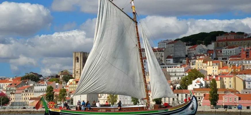 Barco tradicional navegando frente a las coloridas casas de Lisboa