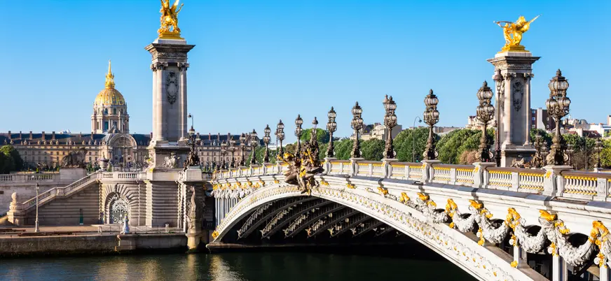 Puente Alexandre III sobre el río Sena en París, con esculturas doradas y farolas ornamentales, bajo cielo despejado.