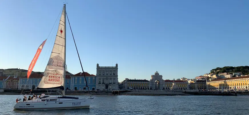 Velero navegando frente a la Plaza del Comercio en Lisboa al atardecer.