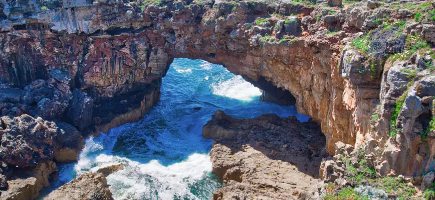 Acantilado de la Boca do Inferno en Cascais con olas rompiendo bajo el arco rocoso.