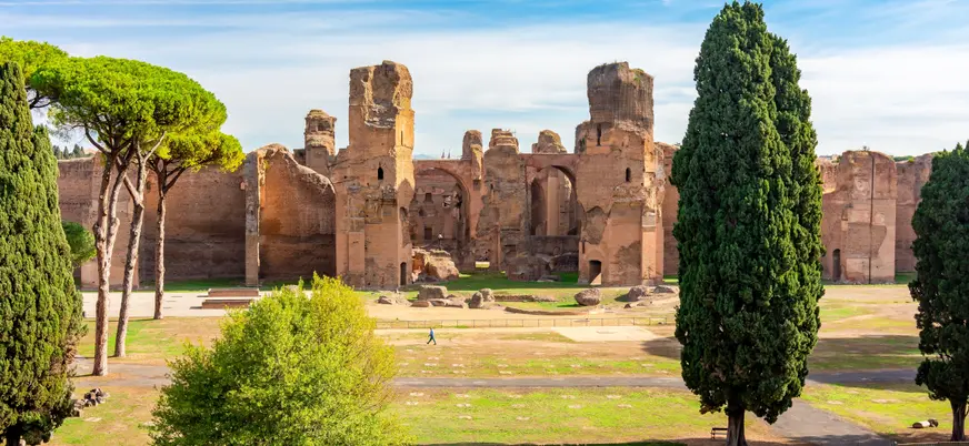 Ruinas de las Termas de Caracalla en Roma, antiguo complejo termal romano rodeado de cipreses y pinos bajo cielo azul.
