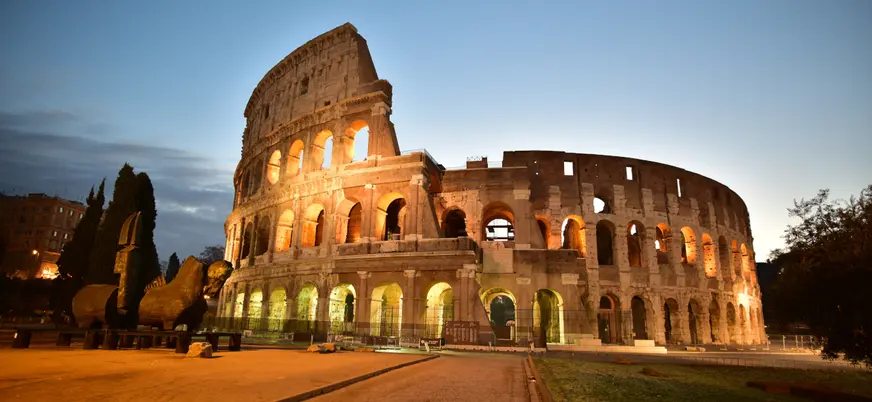 Coliseo de Roma iluminado al anochecer, mostrando su estructura ovalada y arcos icónicos en tonos cálidos.