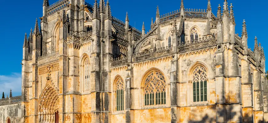 Fachada gótica del Monasterio de Batalha iluminada por el sol bajo un cielo azul.