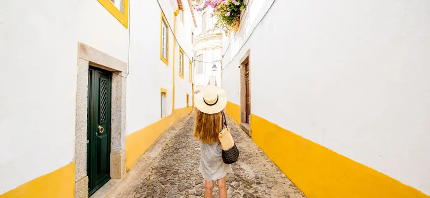 Calle blanca y amarilla de Évora, Portugal, con una turista caminando.