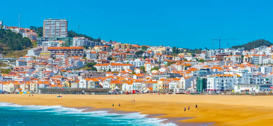 Vista de la playa de Nazaré con casas de tejados rojos y mar azul en un día soleado.