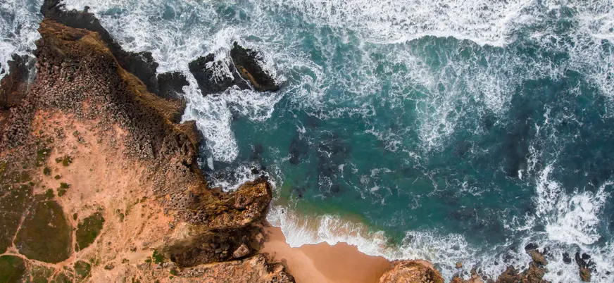 Vista aérea de la playa de Guincho con acantilados y olas rompiendo en la costa.