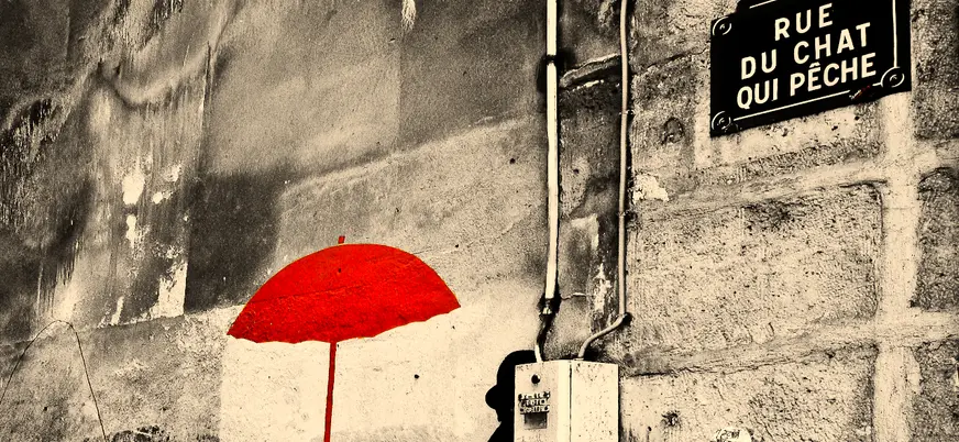 Cartel de la calle Rue du Chat Qui Pêche en París con arte urbano de un paraguas rojo pintado sobre pared antigua.