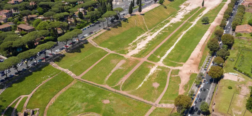 Vista aérea del Circo Máximo en Roma, antiguo hipódromo romano rodeado de árboles y calles, con áreas verdes y restos arqueológicos.