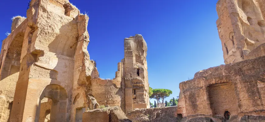 Ruinas de las Termas de Caracalla en Roma, con grandes muros de ladrillo, arcos monumentales y áreas verdes bajo cielo despejado.