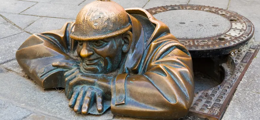 Escultura de Čumil en Bratislava, un hombre de bronce asomando desde una alcantarilla en la acera.