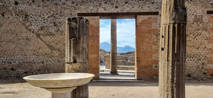 Ruinas arqueológicas de Pompeya con columnas y estructuras romanas, al fondo el monte Vesubio bajo cielo despejado."